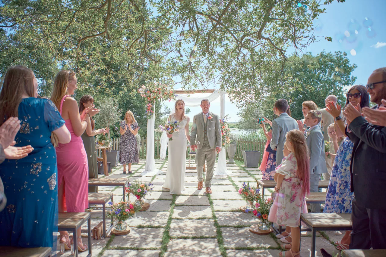 An Amazing image of Bride and groom walking down the isle with bubbles during an outdoor wedding ceremony at Sopley Mill