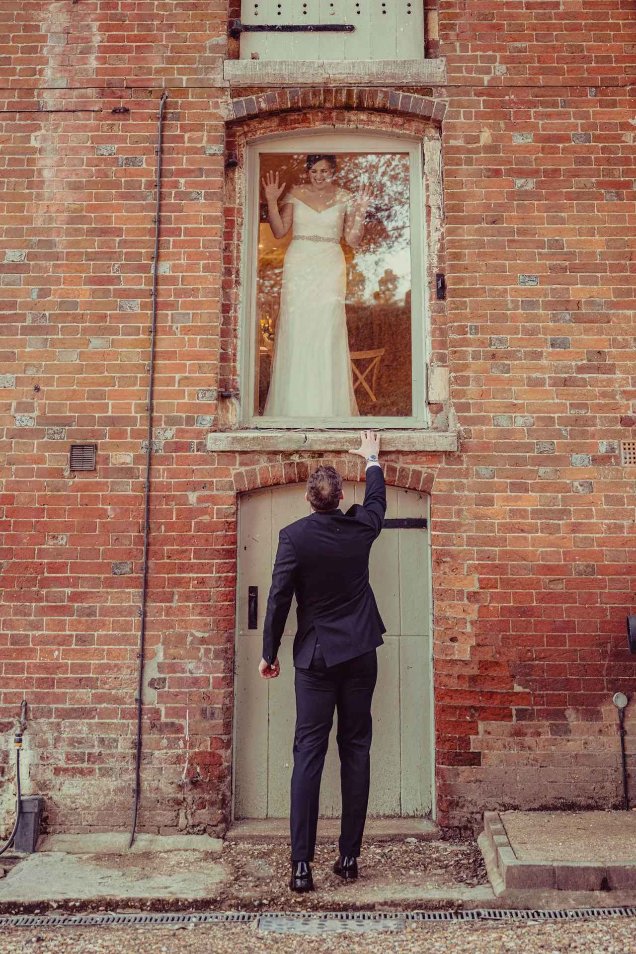 Bride in the window and groom outside in the grounds of Sopley Mill