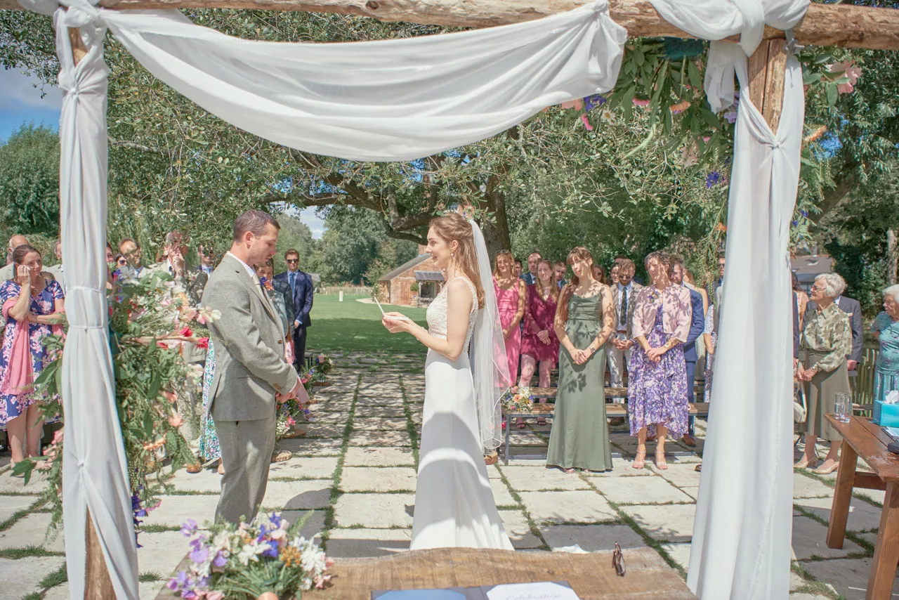 An Amazing light and bright image of Bride and groom reading vows during an outdoor wedding ceremony at Sopley Mill